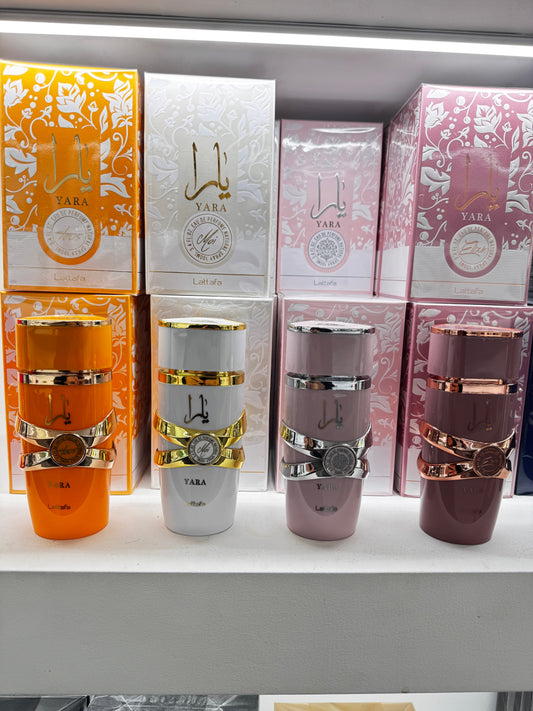 quattro flaconi Yara (rosa, lilla, corallo, viola scuro) affiancati su fondo neutro caldo, luce naturale — stile flat lay da bancone di profumeria. Alt text: "Confronto varianti Yara Lattafa: originale, Moi, Tous ed Elixir